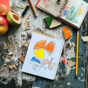 Vue d'une table d'artiste avec des crayons, des découpages colorés, un carnet ouvert et des fruits, illustrant un atelier créatif du cours de perfectionnement en art-thérapie.
